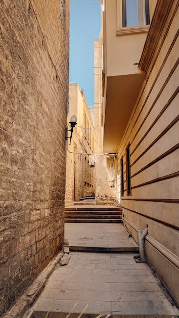 A narrow cobbled street in Pimlico, enclosed by tall brick buildings on either side, with a flight of weathered stone steps leading upward at the end of the alley. The steps are flanked by black metal